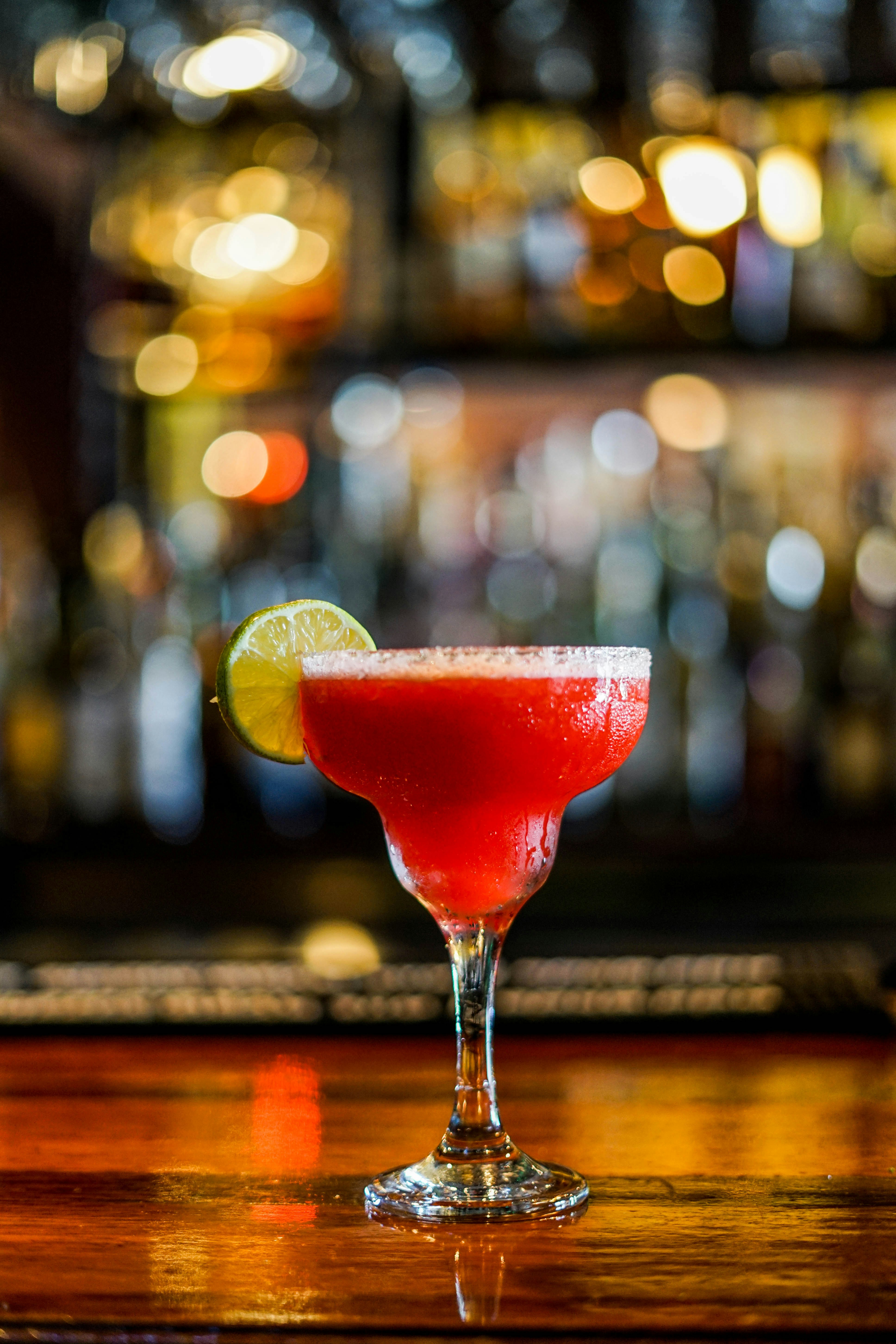 A red margarita with a salted rim and lime against softly glowing bar lights